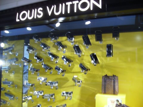 Pic of a storefront display of a pricey purse being the focus of multiple surveillance cameras